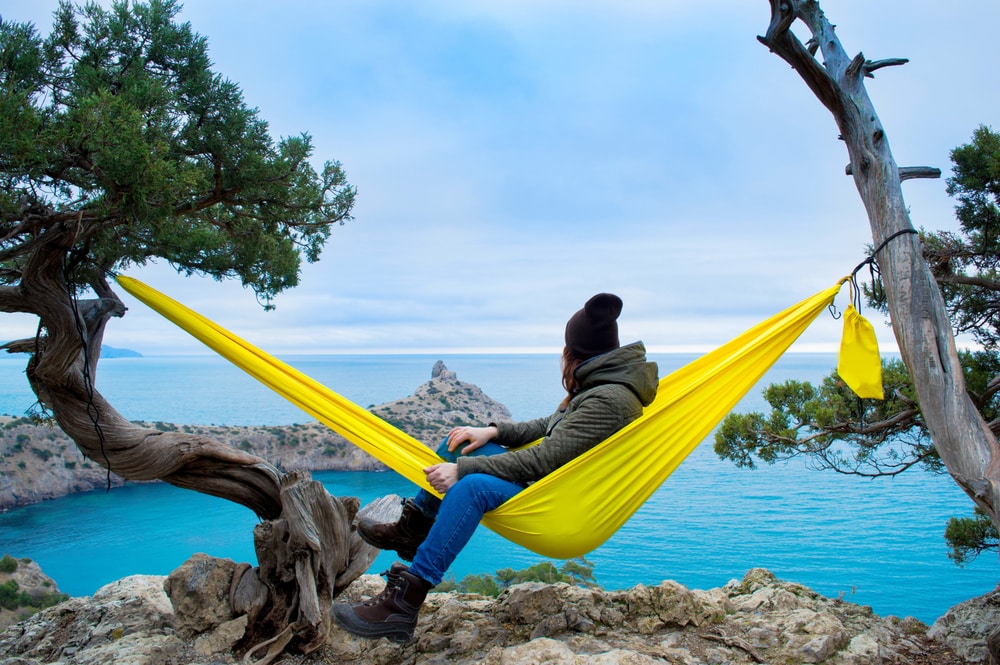 Woman relaxing in the yellow turquoise hammock against the backdrop of a beautiful landscape. Concept of relaxation and meditation. The southern coast of the Crimea in winter. New world (Novyi Svet)